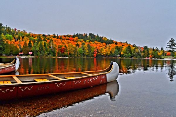Fall view of a dock on a Muskoka lake with calm water and autumn trees along the shoreline”
